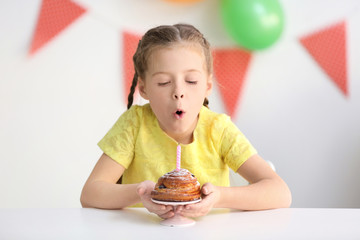 Cute little girl blowing out candle on birthday cake at home