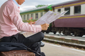 travelling concept.Relax time of businessman traveler holding location map and looking for some direction, waiting for a trains at train station,selective focus,vintage color