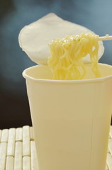 soft boiled instant noodles with smoke on plastic fork from white paper cup