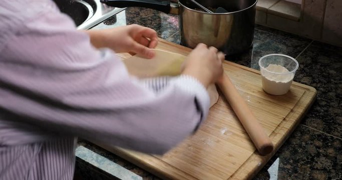 Female hands spreading out meat and spices on freshly rolled dough and cutting to make meat pies 