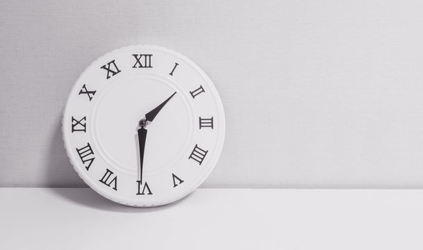 Closeup white clock for decorate show half past one o'clock or 1:30 p.m. on white wood desk and wallpaper textured background in black and white tone with copy space