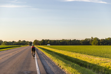 Road cyclist riding by open fields