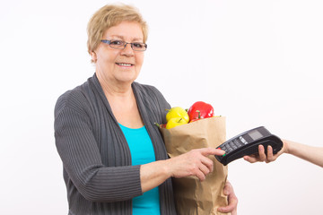 Senior woman holding shopping bag and using payment terminal, enter personal identification number