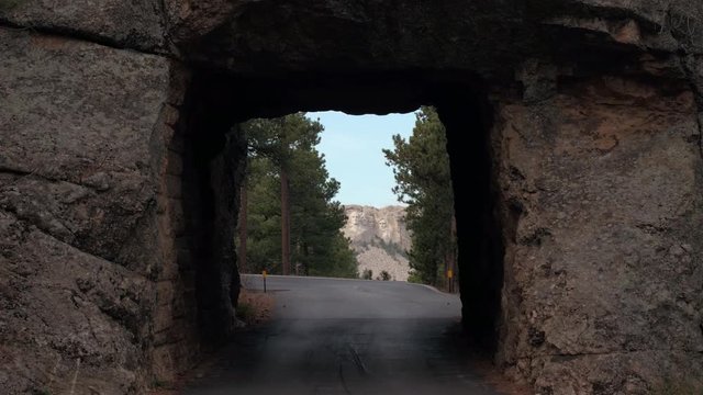 SLOW MOTION: Great vista point from the Narrow single lane tunnel in granite rock face revealing scenic view of the iconic Mount Rushmore monument in Black Hills, South Dakota. Four famous presidents