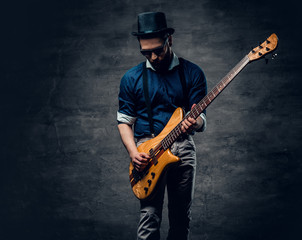 Studio portrait of the hipster bass player dressed in cylinder hat.