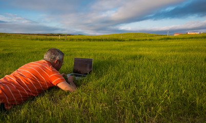 Man with laptop in a meadow at sunset