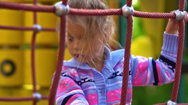 Young girl climbing on a rope climbing frame on a sunny day in slow motion