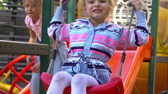 Children ride on the swings at the playground. Slow motion