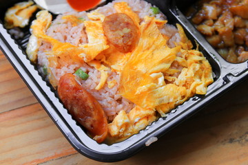 omelet with sausage pork on fried rice close up  in box black Thai style food wood table background