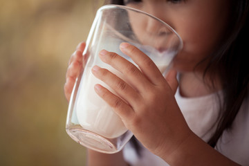 Closeup child hand holding and drinking a milk from glass in vintage color tone