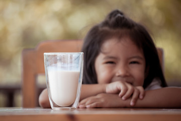 A glass of milk on table with blur asian little girl on background in vintage color tone