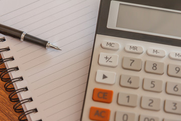 Blank notebook with pen and calculator on wooden table, business concept