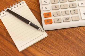 Blank notebook with pen and calculator on wooden table, business concept