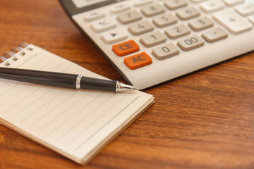 Blank notebook with pen and calculator on wooden table, business concept