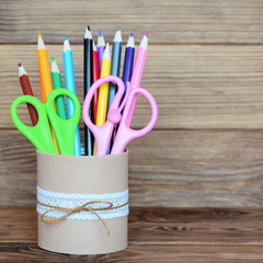 Colored pencils and scissors in a decorative tin can. Recycled tin can for storage of stationery isolated on wooden background. Closeup