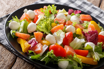 Hearty salad with salmon, mozzarella and fresh vegetables close-up on a plate. horizontal