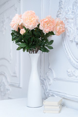 Artificial pink peonies in a white vase next to white books. Composition of flowers in a white vase