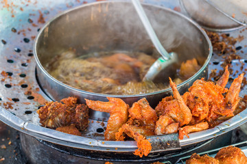 Thai style crispy deep fried chicken wings for sale in Thailand market. Cooking in heat oil in a large deep fryer.