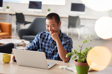 Smiling Asian designer working on a laptop in an office