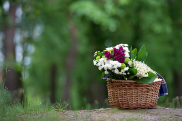 A magnificent bouquet of lilies of the valley and other flowers in a wooden basket in the background of the forest