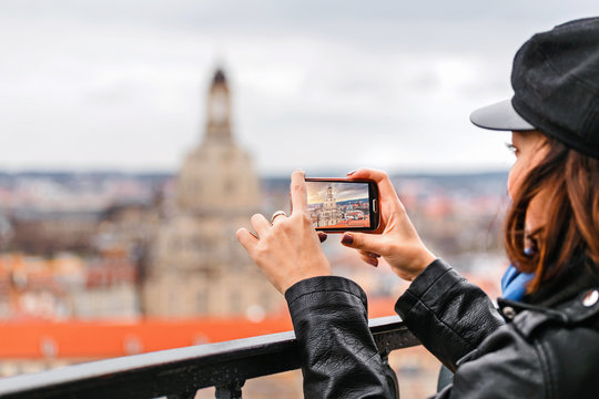 Young woman taking a photo on her smartphone of a Dresden city with Frauenkirche landmark