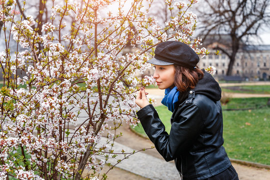 Woman in cap and leather jacket with cherry flowers in spring park