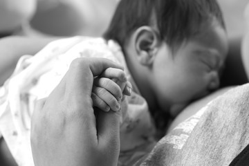 Close-up of mother's holding baby's hand with tenderness, focus at baby hand, black and white
