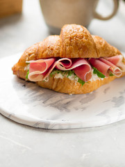 Croissant with ham and salad on a white ceramic board