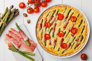Tart with asparagus and tomatoes on white wooden background.