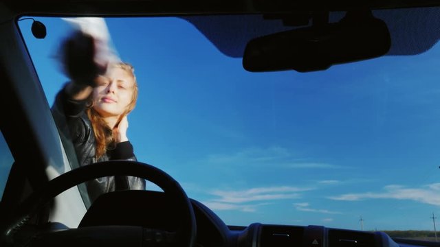 Young attractive woman wiping the windshield of a car. View from inside the car. Against the background of a red blue sky on a clear day