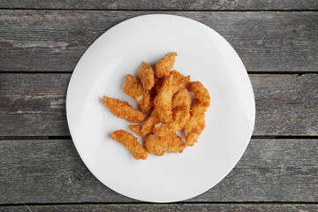 Crisp grilled chicken wings on a white dish on wooden table, top view.
