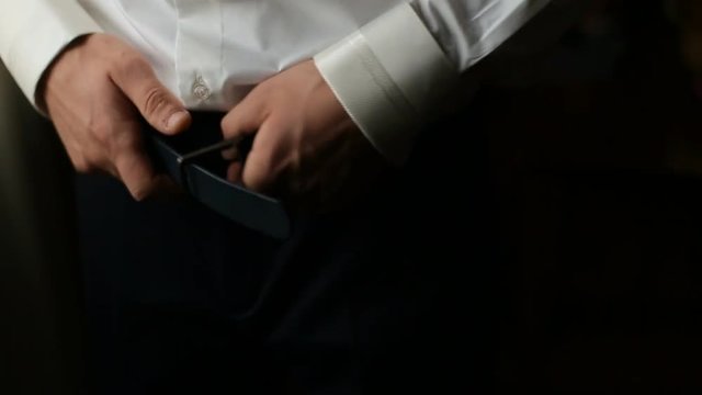 Groom puts belt on his pants before wedding ceremony. Man buckling belt on his pants. Close up