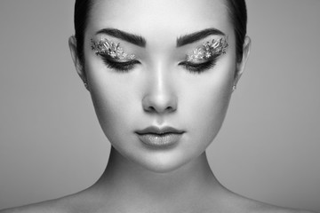 Fototapeta premium Young beautiful woman with flower makeup eyes. Spring makeup. Beauty fashion. Eyelashes. Cosmetic Eyeshadow. Make-up detail. Girl on green background. Black and White photo