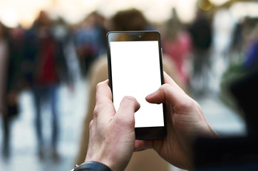 Photo of a man's hands holding smartphone with blank display with blurred people walking in the street in the background