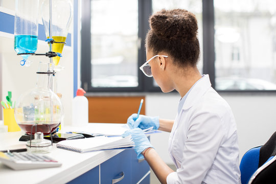 Young scientist in eyeglasses making experiment and taking notes in research laboratory