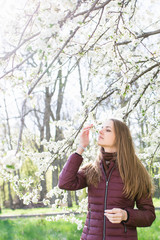 Beautiful caucasian girl smells the blooming of a cherry in a flowering garden.