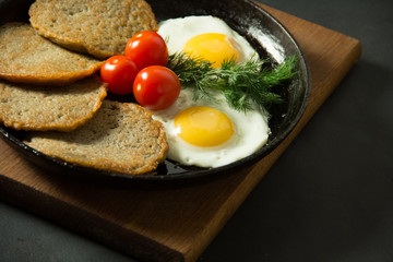 Homemade food. Tasty breakfast. Appetizing fried egg with potato pancakes and herbs in dripping pan  on a black background