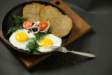 Homemade food. Tasty breakfast. Appetizing fried egg with potato pancakes and herbs in dripping pan  on a black background