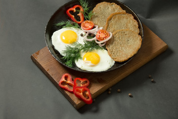 Homemade food. Tasty breakfast. Appetizing fried egg with potato pancakes and herbs in dripping pan  on a black background.