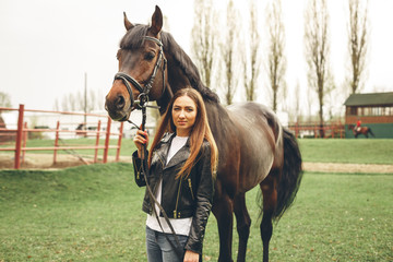 Obraz premium Beautiful girl communicates with the horse in the park. Preparing for the riding