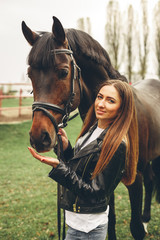 Obraz premium Beautiful girl communicates with the horse in the park. Preparing for the riding