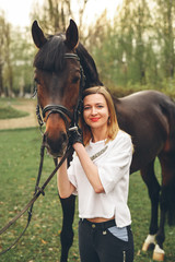 Beautiful girl communicates with the horse in the park. Preparing for the riding