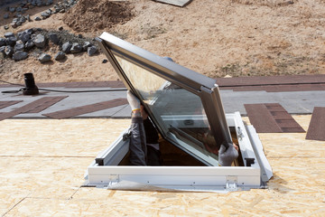 Worker on a asphalt shingle roof installing new plastic (mansard) or skylight  window