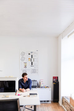 Mid adult man sitting at desk in office looking out of window