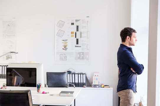 Side view of mid adult man in office arms crossed looking out of window
