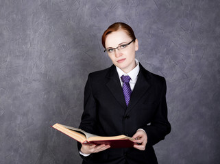 Female lawyer holding a big book with serious expression, woman in a man's suit, tie and glasses