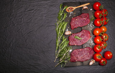 Raw beef steak on a cutting board with vegetables and spices.