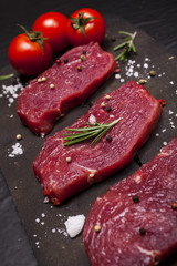 Raw beef steak on a cutting board with rosemary and cherry tomatoes.