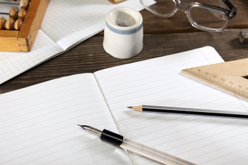 A penholder  with a pen ,a simple pencil,straightedge, abacus  and glasses lie on an open notebook. Retro stylized photo. View from above. Close-up.