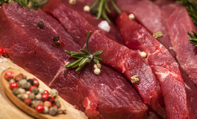 Raw beef steak on a cutting board with rosemary and spices.